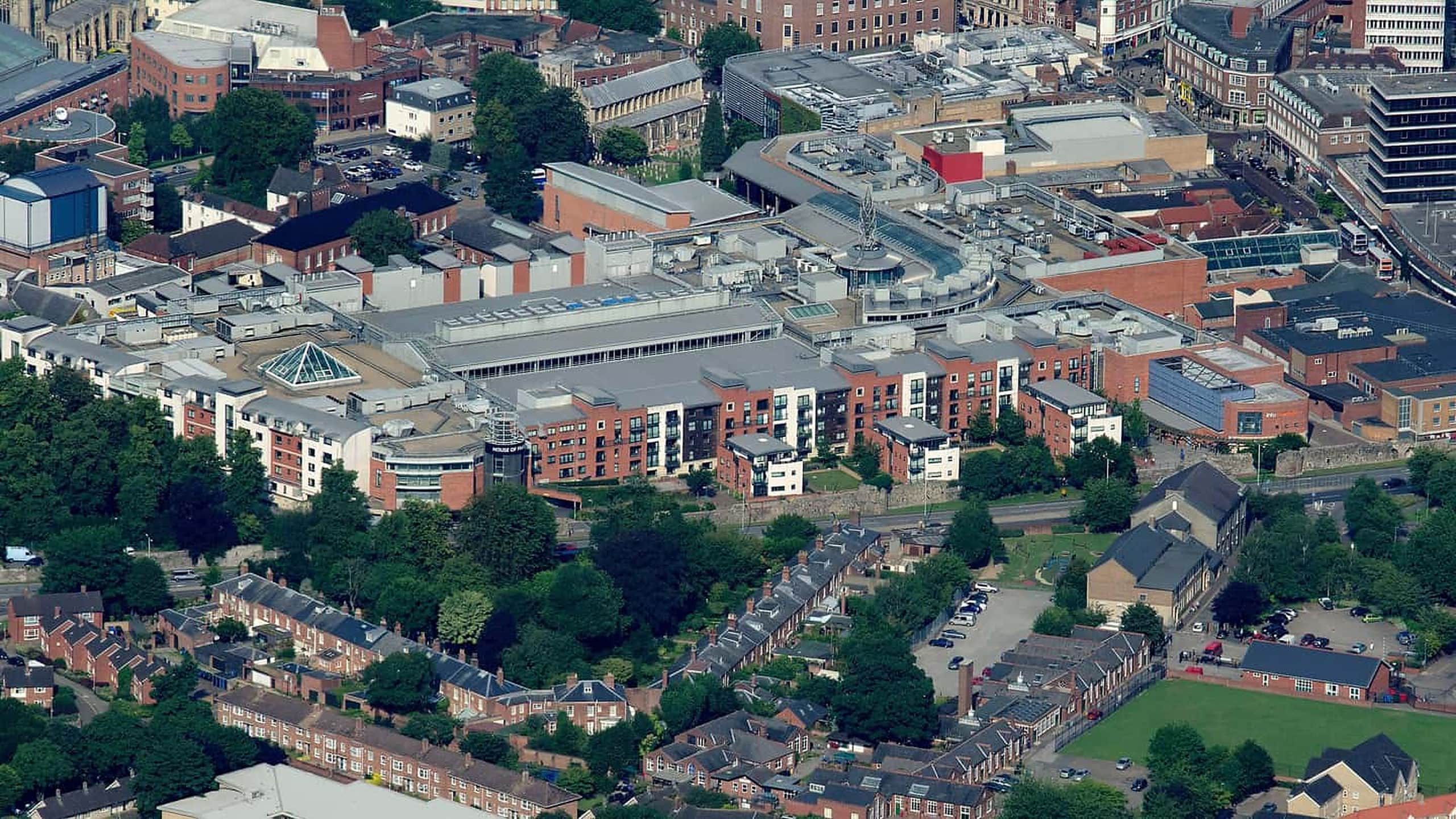 Aerial photograph of a downtown retail block: a wide low-slope roof carrying rows of rooftop mechanical units and skylights, ringed by apartment buildings and rows of brick townhouses.