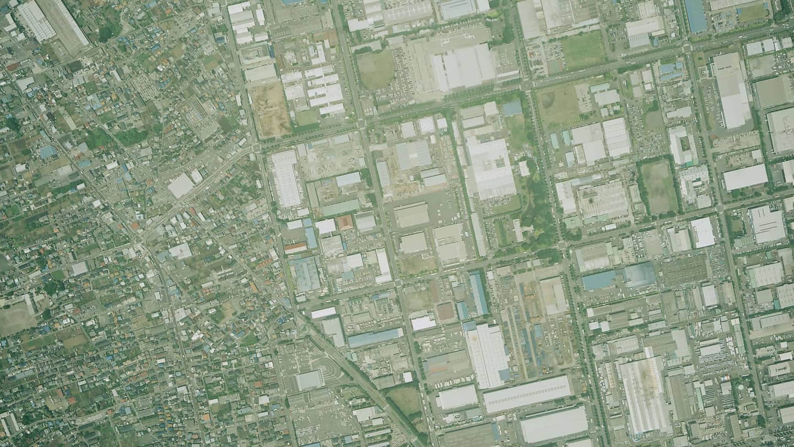 Vertical survey photograph of an industrial park: rectangular plant buildings, yards, and vacant lots laid out on a road grid, with a dense low-rise residential district along one edge.