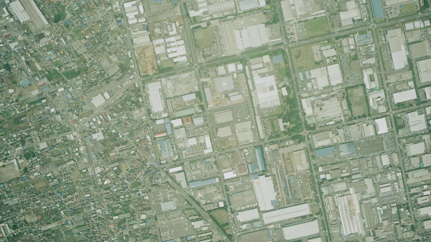 Vertical survey photograph of an industrial park: rectangular plant buildings, yards and vacant lots laid out on a road grid, with a dense low-rise residential district along one edge.