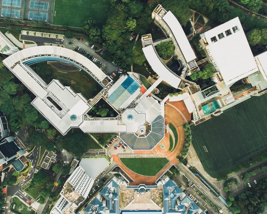 Aerial photograph looking straight down on a campus of pale curved roofs, courts, and planted ground.