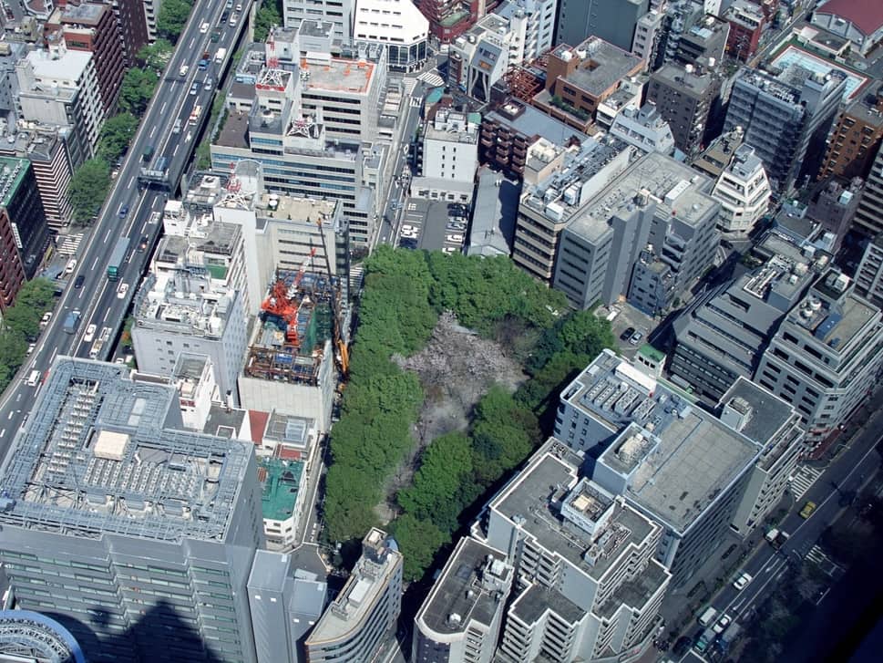 Aerial photograph of a dense city block: office rooftops, an elevated road, and a wooded courtyard.